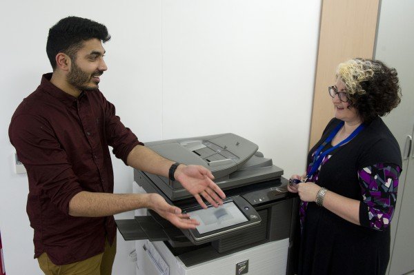 Colleagues chat at a photocopier.