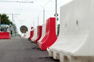Red and white mobile plastic water filled jersey barriers for temporary limit no access work zone highway parking roadblock.